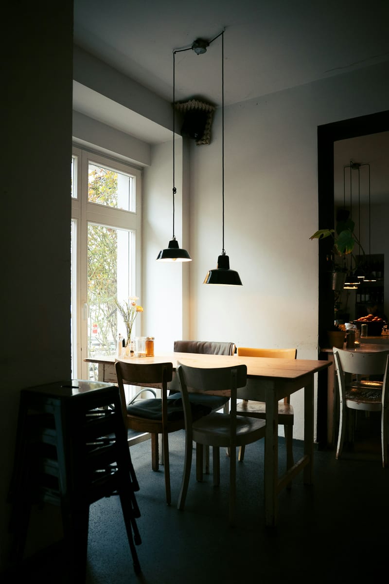 Berlin'de sade bir kafe ic mekani; pencere kenarinda masalar ve sandalyeler, gunisigi dolu bos salon.