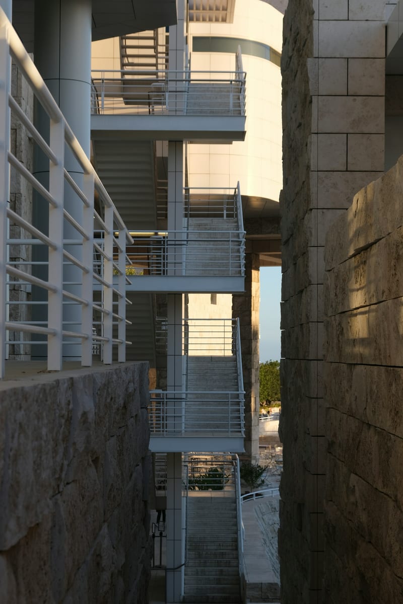Getty Center'in travertin tas kaplamali dis merdiven detayi; bej notr palet, dogal gunduz isigi, geometrik mimari yakin plan.