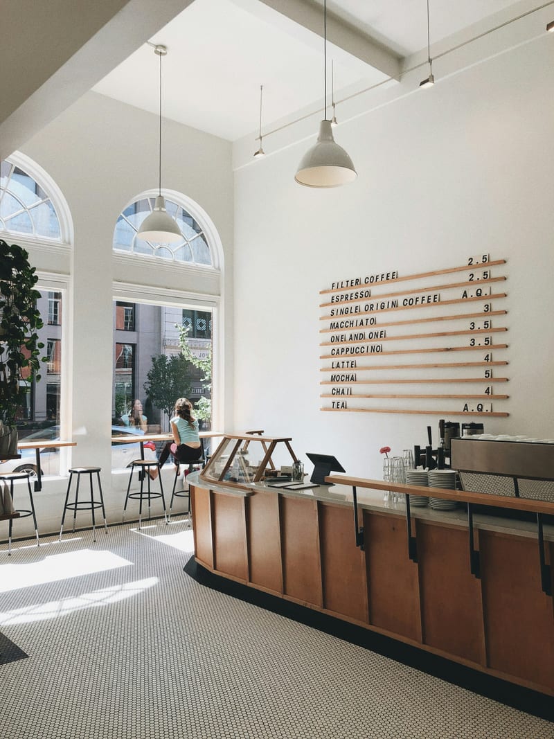 Kavisli tezgahli modern kahve dukkani ic mekani. Insan yok, okunan tabela/logo yok. Notr gri ve kirik beyaz baskin, dusuk doygunluk. Net odak, iyi pozlanmis. Kucuk butik kafe salonu olarak okunuyor; tezgah + arkasindaki sade duzen goruluyor. Ucretsiz Unsplash Lisansi.