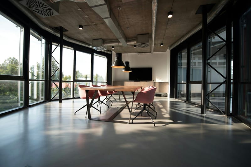 Genis pencerelerden gelen gunisiginin masaya golge dusurdugu bos toplanti odasi.
